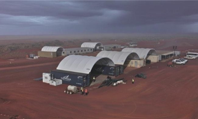 DomeShelter™ structures at remote mining site under cloudy sky in red dirt landscape.
